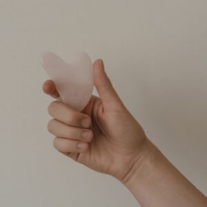 Homepage New A hand holds a rose quartz gua sha tool against a neutral background, showcasing skincare elements.