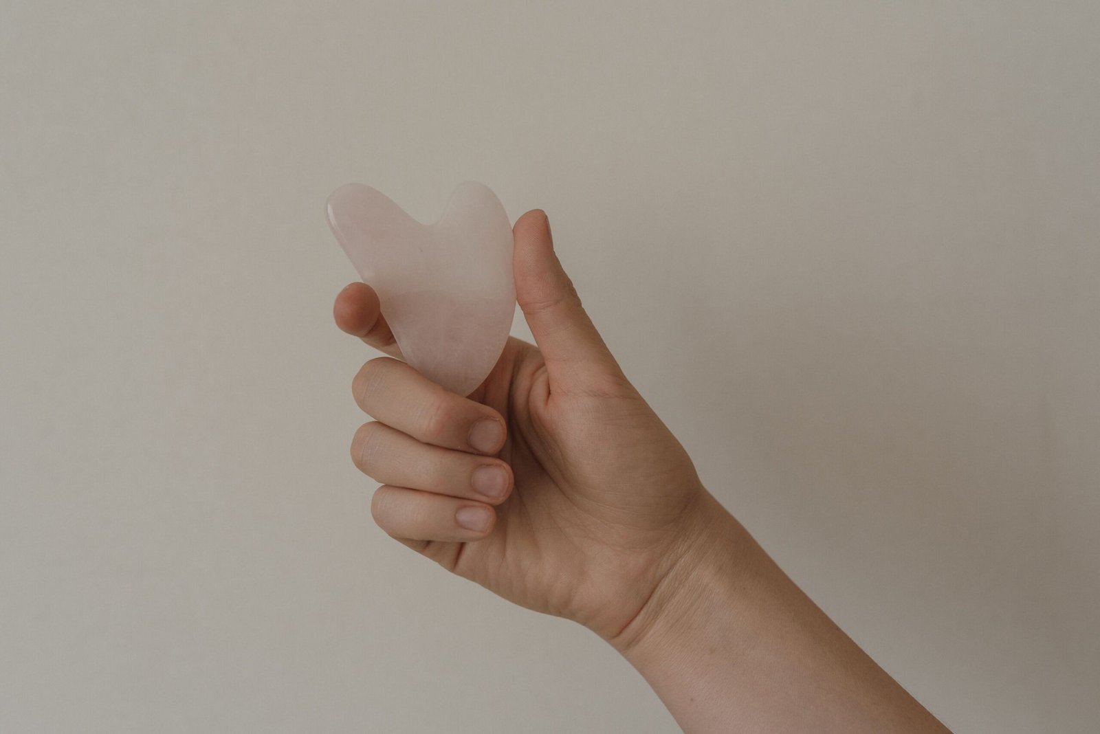 pexels photo 6663588 6663588 A hand holds a rose quartz gua sha tool against a neutral background, showcasing skincare elements.